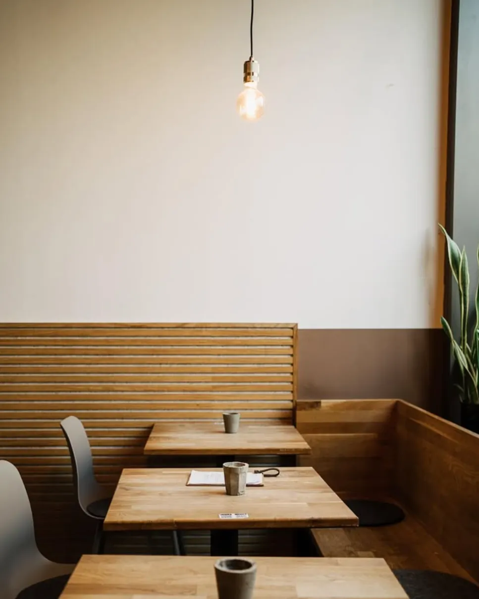 Wooden tables with ceramic cups under a warm light bulb at noy