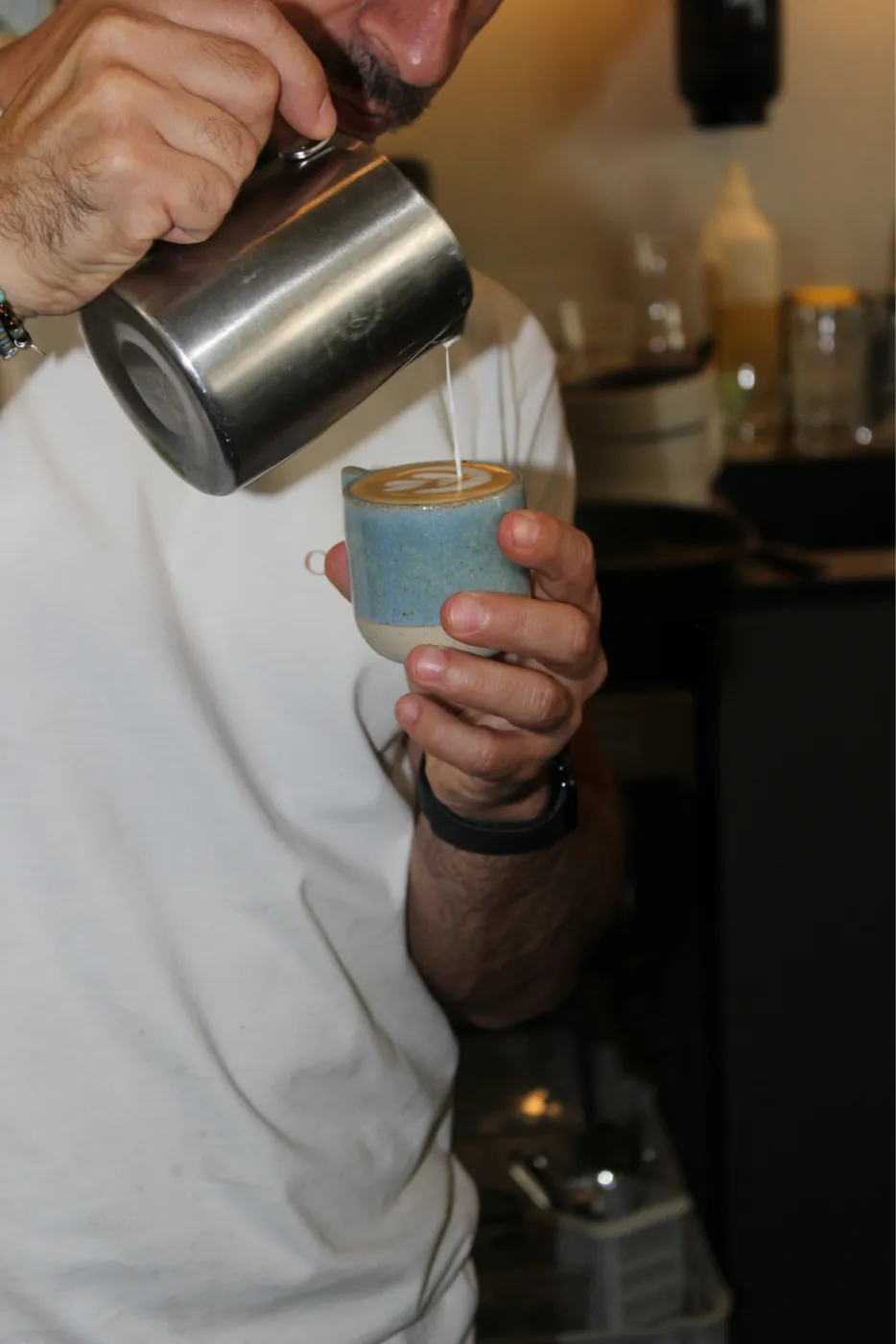 Barista pouring latte art into a blue espresso cup