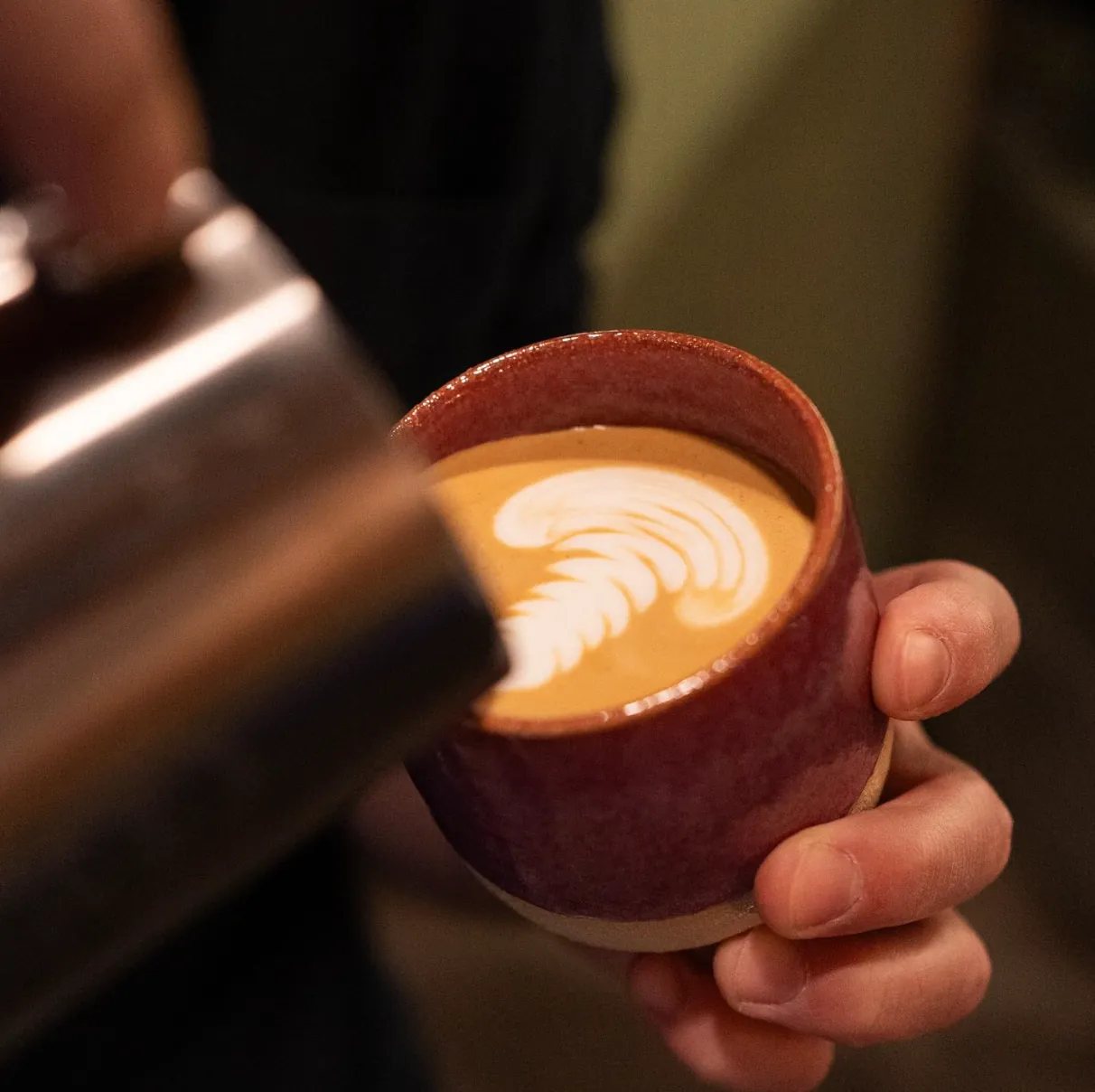 Barista pouring latte art into a red ceramic cup